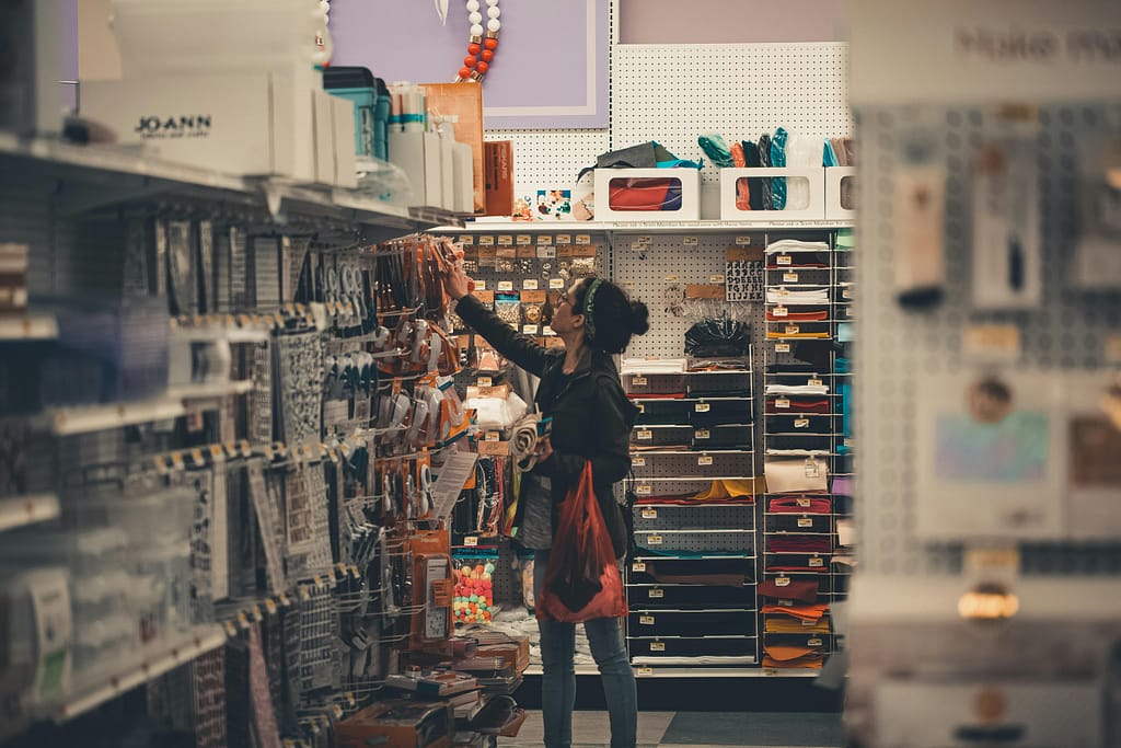 Woman reaching for items in a busy craft store aisle, exploring various art supplies.